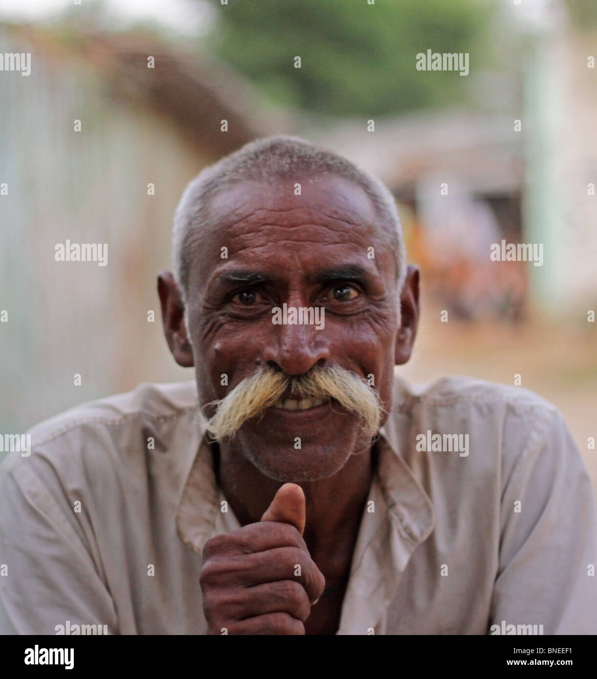 An Old Indian man sitting on a cot outside his house and smoking a hookah in a remote village in India Stock Photo