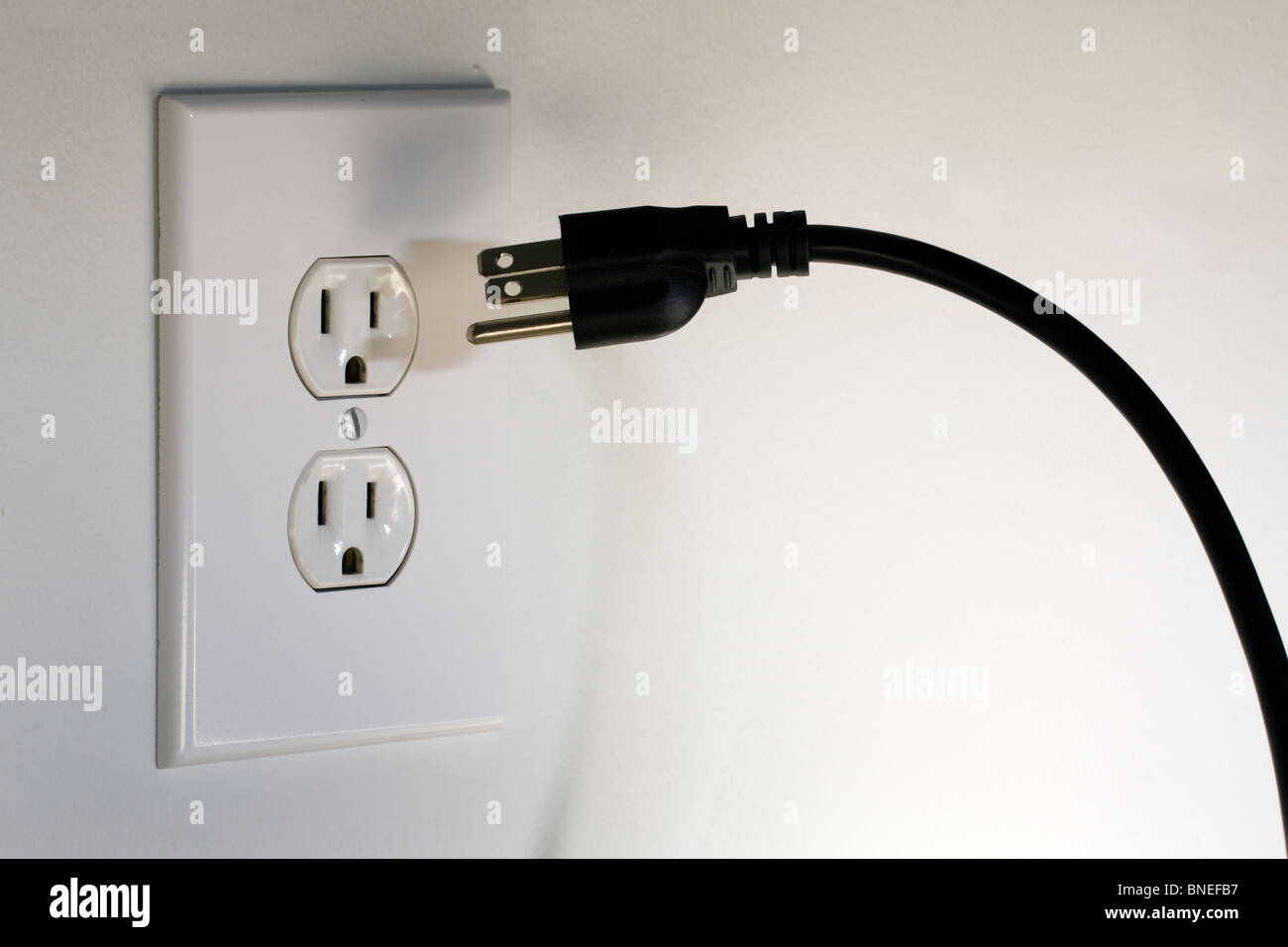 American Three Pronged Plug hovering in front of a 110 Volt A/C Electrical Outlet Stock Photo