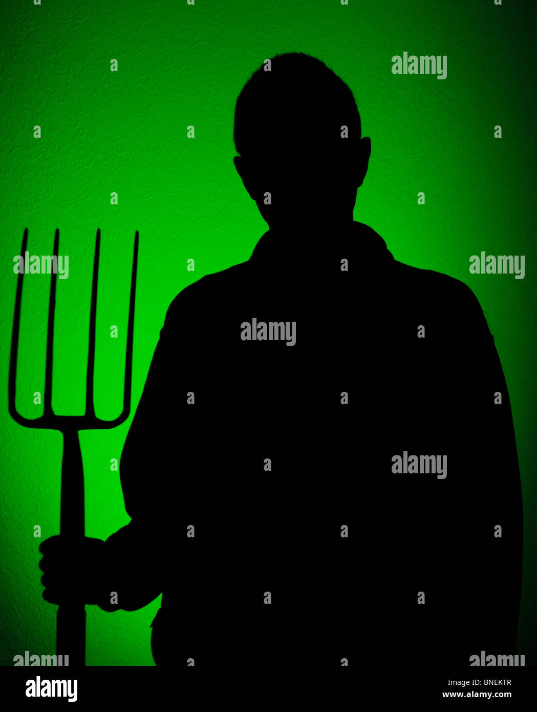 Silhouette of a man holding a garden fork against a green background Stock Photo