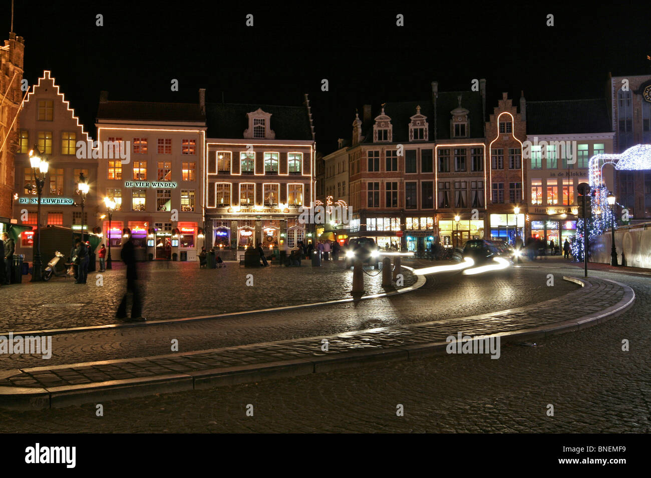 View of the Western side of the Markt at night with the cobbled street of Steenstraat in the foreground and passers-by Stock Photo