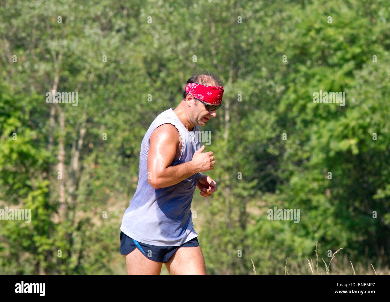 A bald man with a red bandanna running. He is covered in sweat Stock