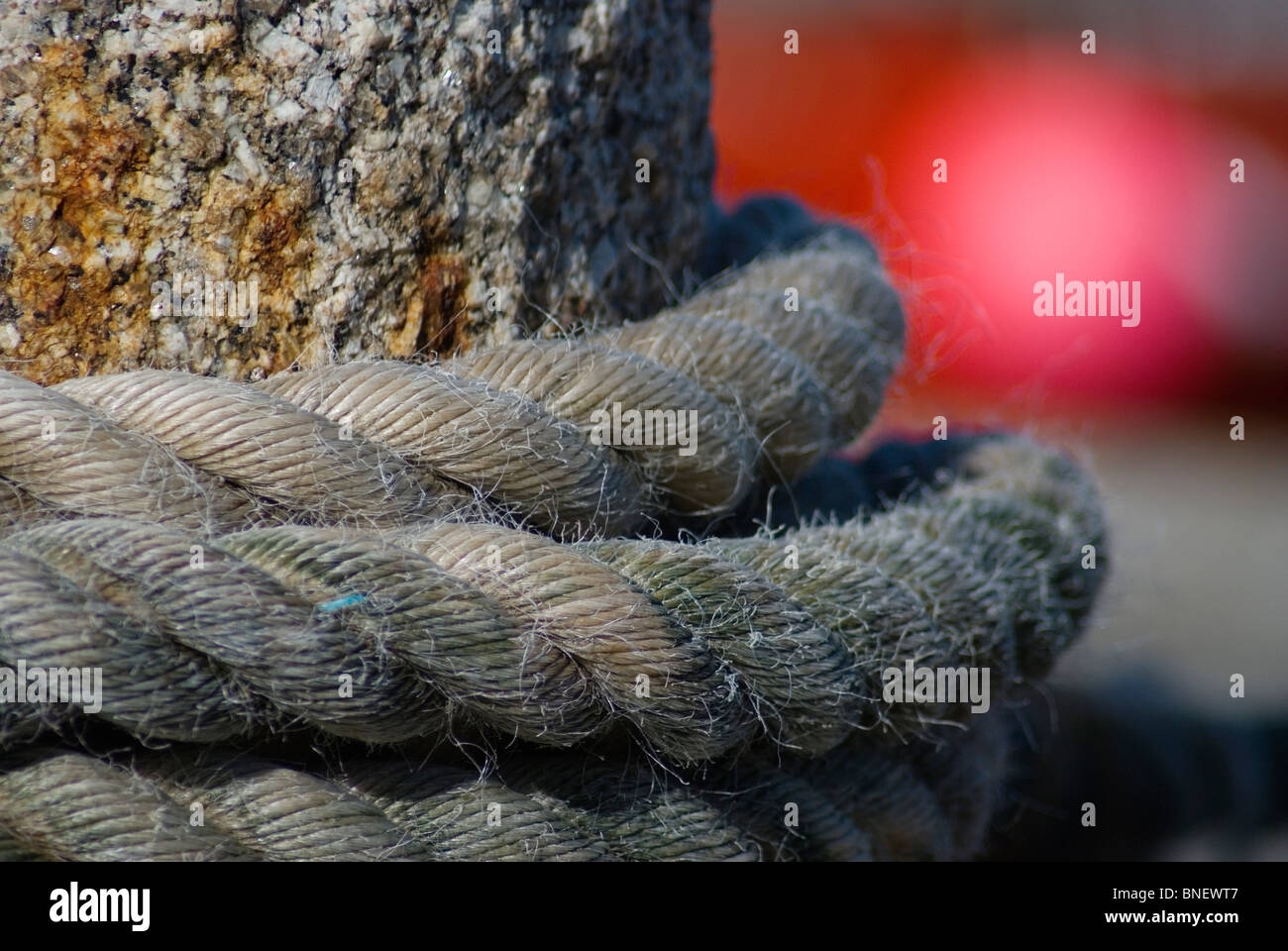 Mooring rope tied around a granite bollard on the harbour wall at