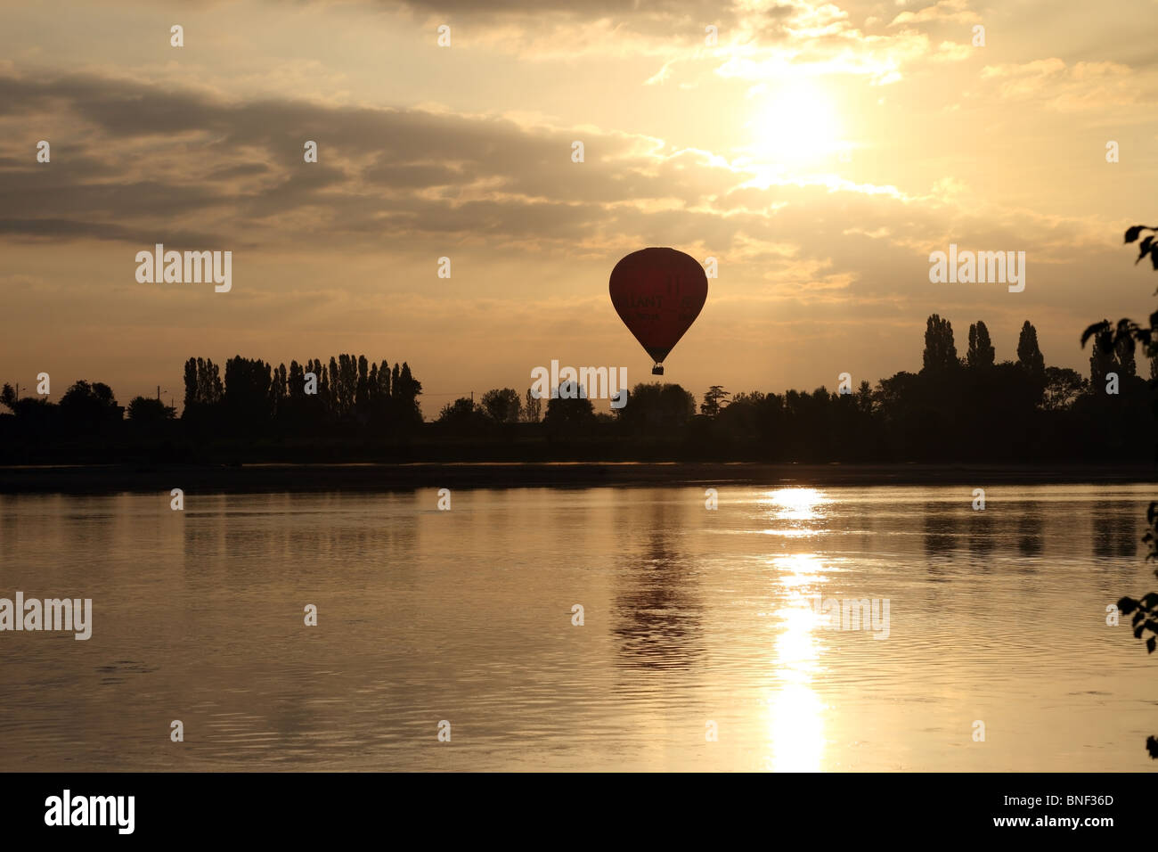 Hot Air Balloon Flying Over the Town of Les Rosiers Sur Loire Just After Sunrise With the Loire River in the Foreground France Stock Photo