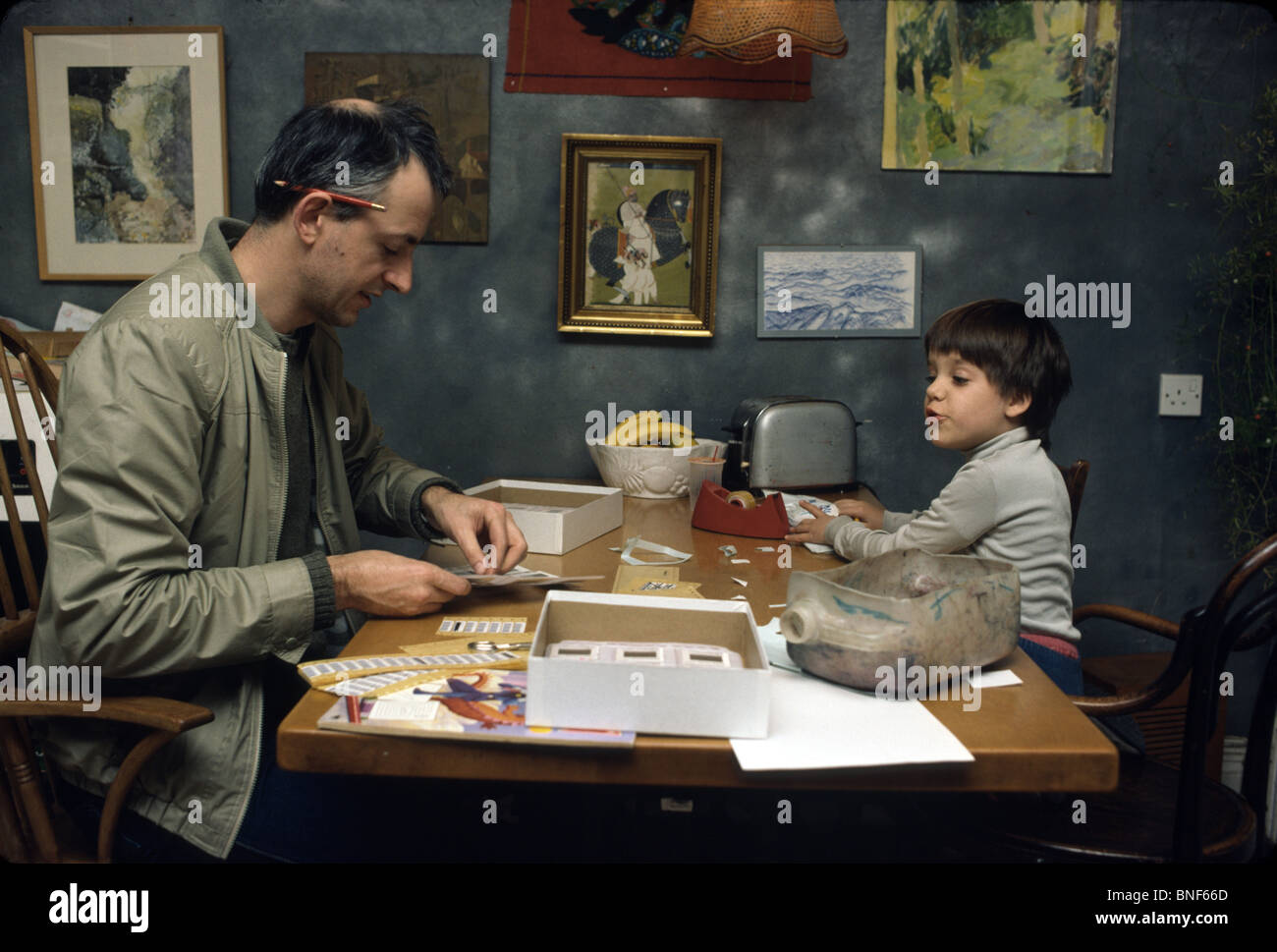 archive image of father doing work at the kitchen table with his daughter playing Stock Photo