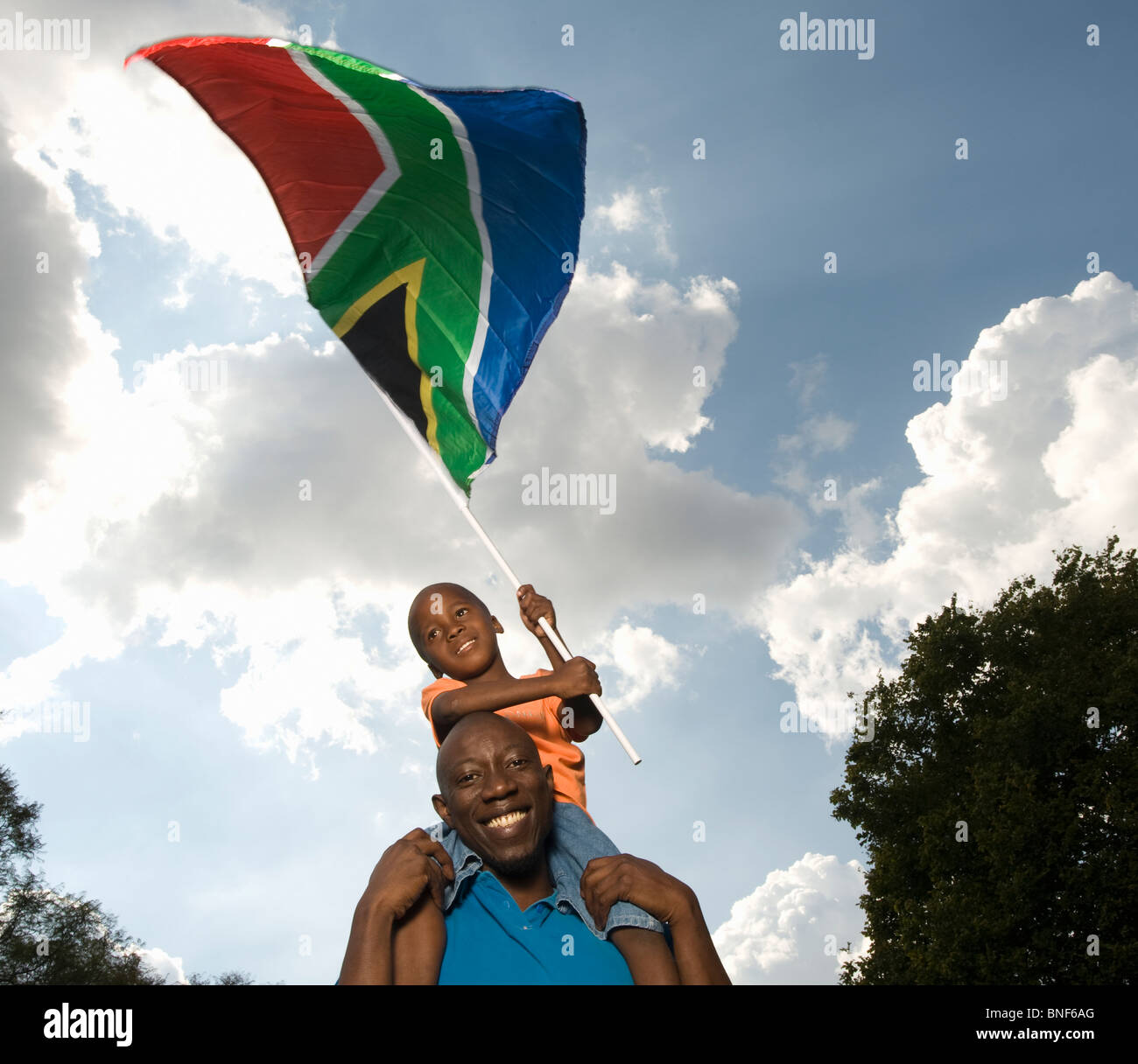 Father carrying son (4-5) on shoulders, waving South African Flag, Johannesburg, Gauteng Province, South Africa Stock Photo