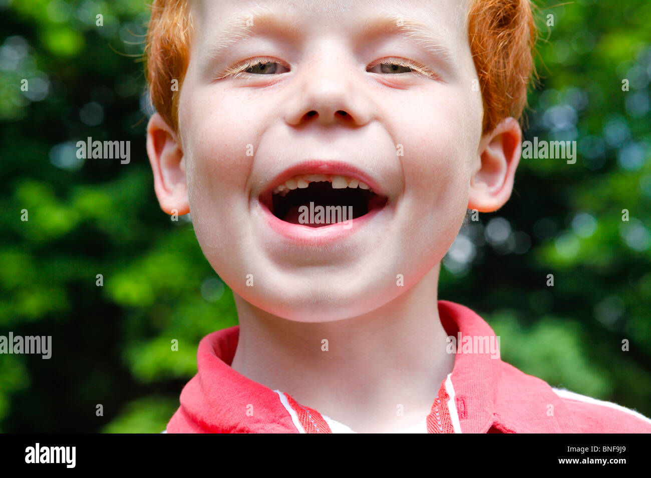 A six yeal old boy smiles showing his missing child tooth and his adult tooth growing through, in the garden. Stock Photo