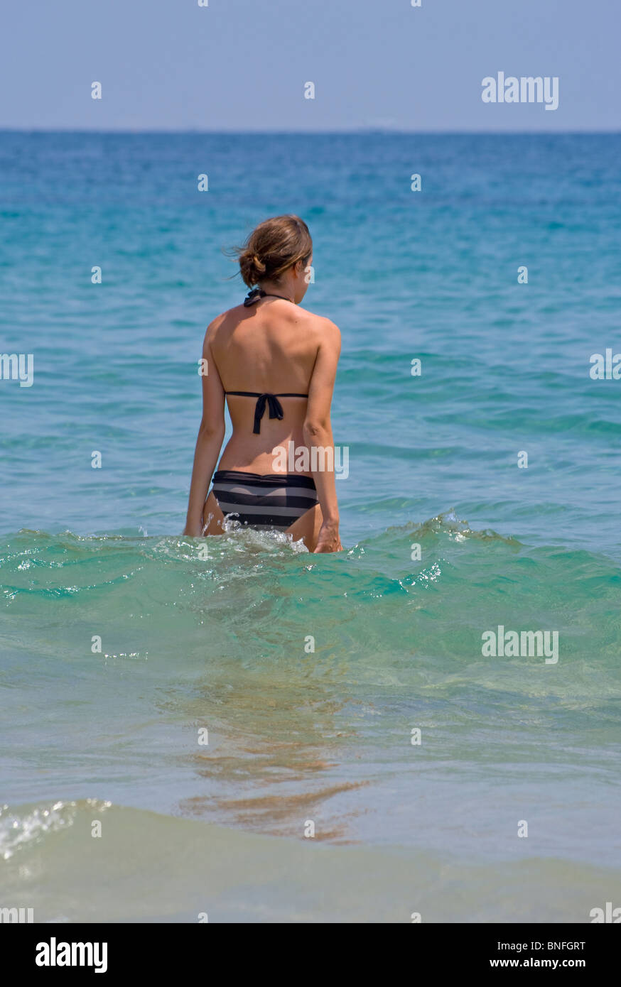 Young Slim Woman In A Bikini Walking Into The Sea Stock Photo