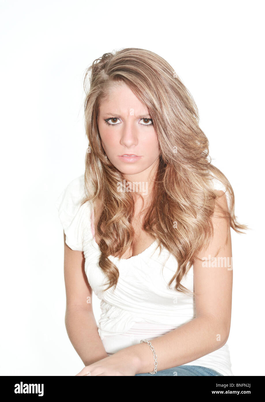 A pretty, teenage girl sits and glowers at the camera as if she's angry. Conceptual Stock Photo