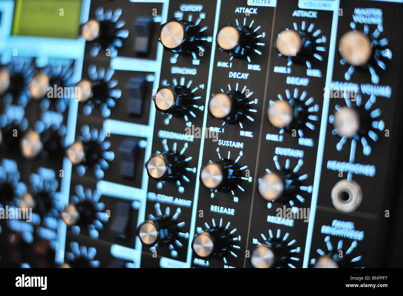 Angled photo of a Moog Synthesizer with blurred foreground and background.  Knobs, switches and blue backlit control panel. Stock Photo