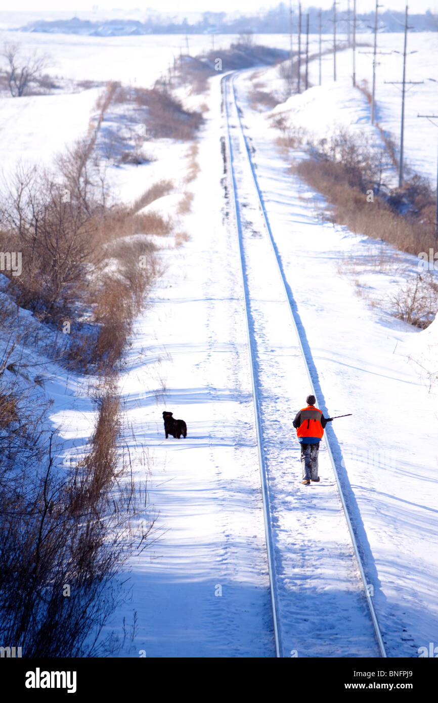 A hunter and his dog walk down a set of railroad tracks to find their