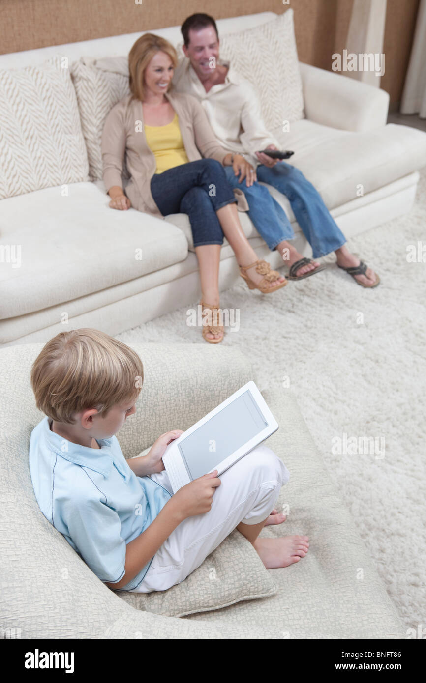 Parents watch television while son reads a digital book Stock Photo