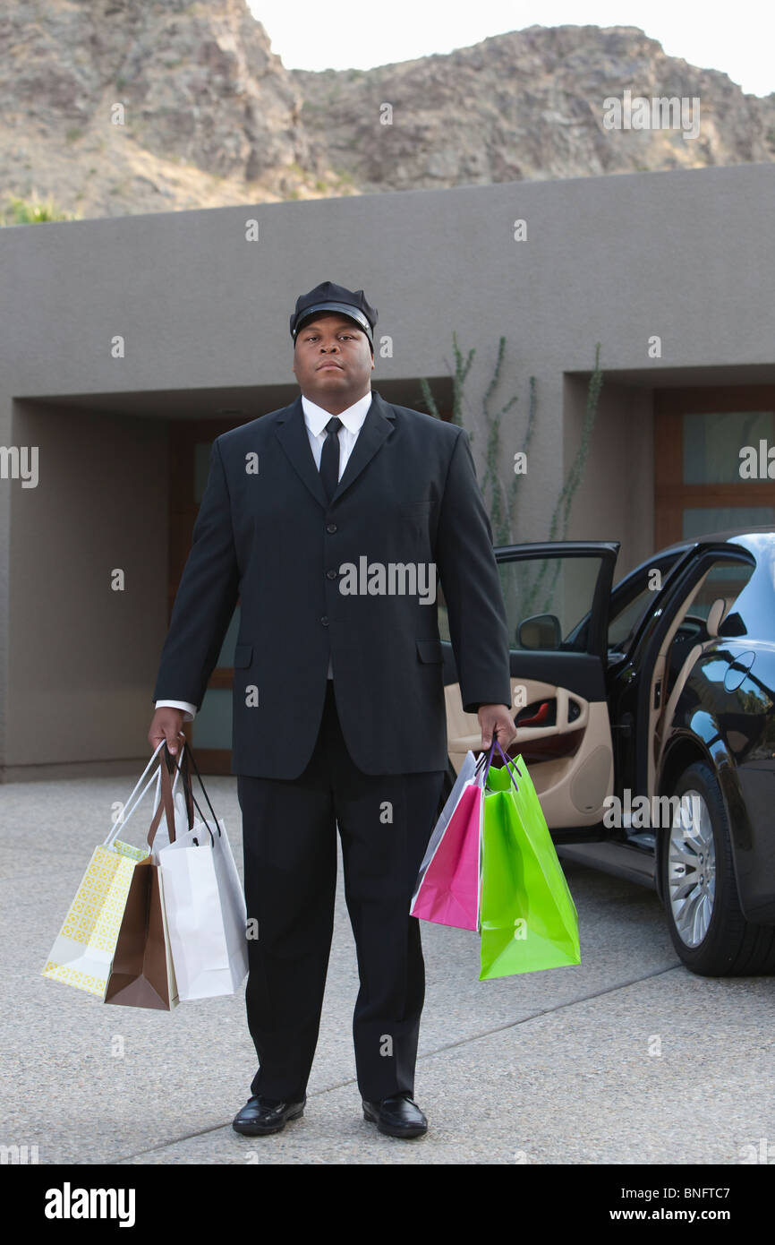 Chauffeur holds shopping bags in driveway near luxury vehicle Stock Photo