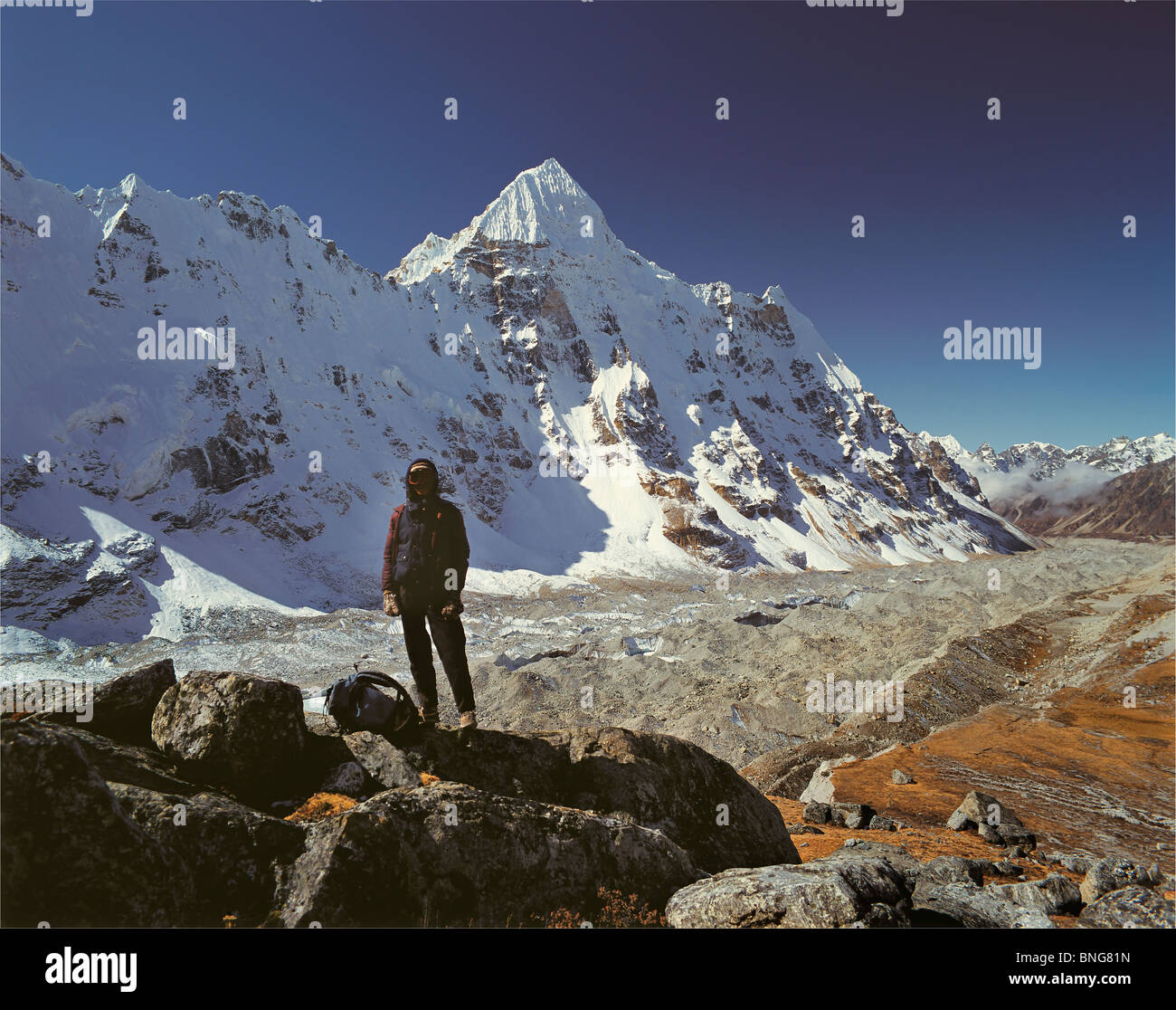 A Nepali porter stands on a rocky outcrop with Wedge Peak and the Kangchenjunga Glacier behind, east Nepal Stock Photo