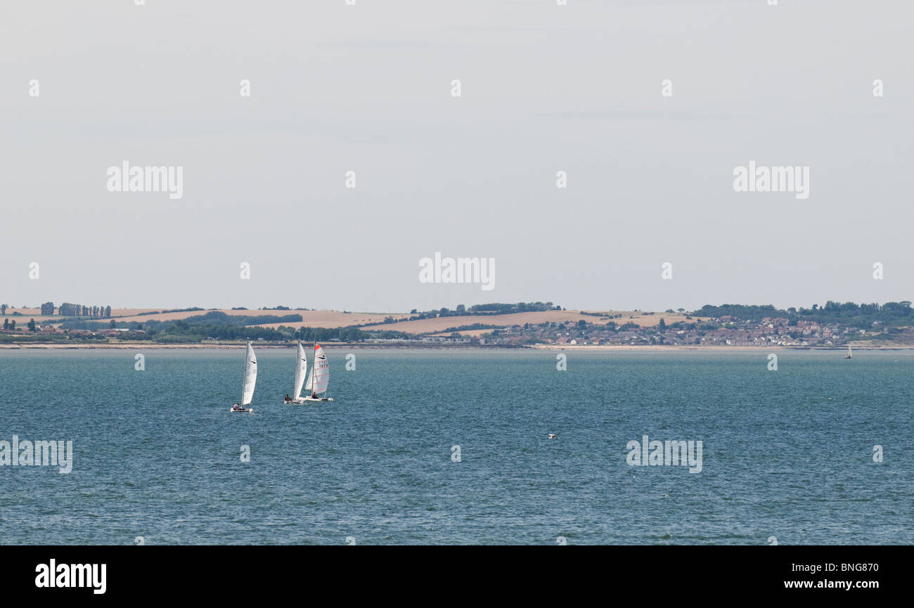 Three sailboats off the coast at Whitstable in Kent. Stock Photo