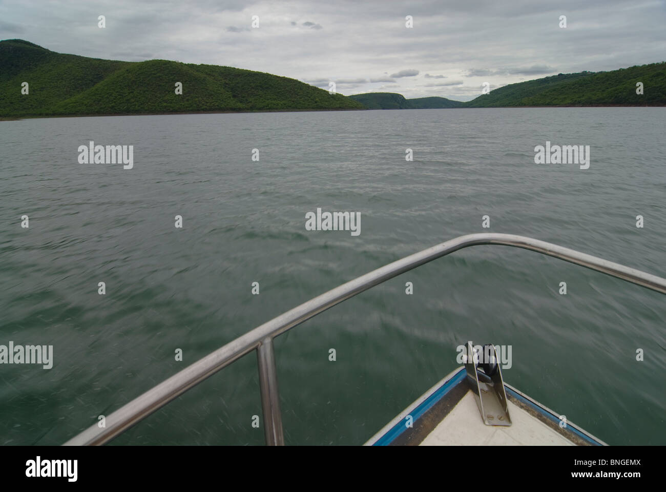 Motion blur in lower areas of water with over cast sky above. High angle of a boats bow surrounded by water. Two pieces of land joined by a dam wall. Stock Photo