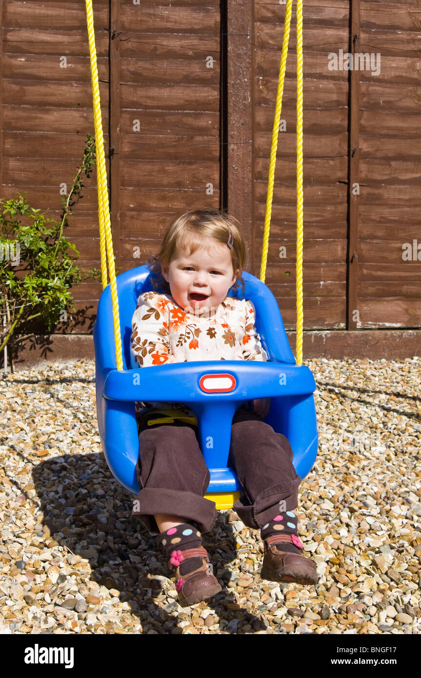 Vertical portrait of a little girl having great fun being pushed in a swing in the back garden. Stock Photo