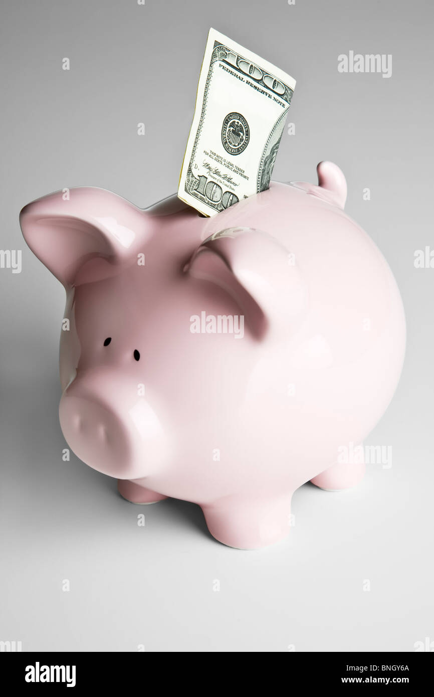 100 dollar bill sticking out of the coin slot of a pink piggy bank Stock Photo
