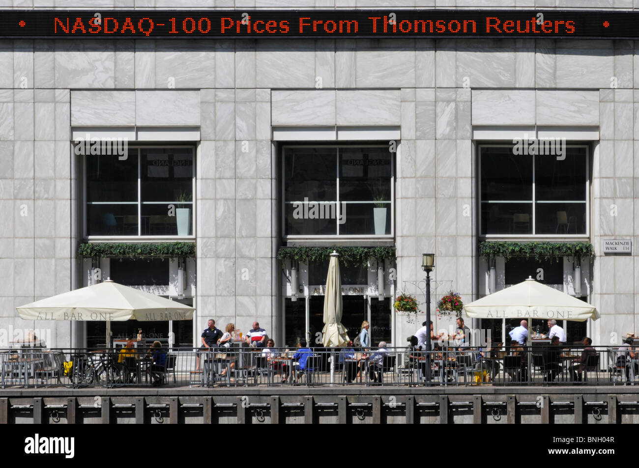Canary Wharf Thomson Reuters electronic Nasdaq sign above outdoor bar Stock Photo