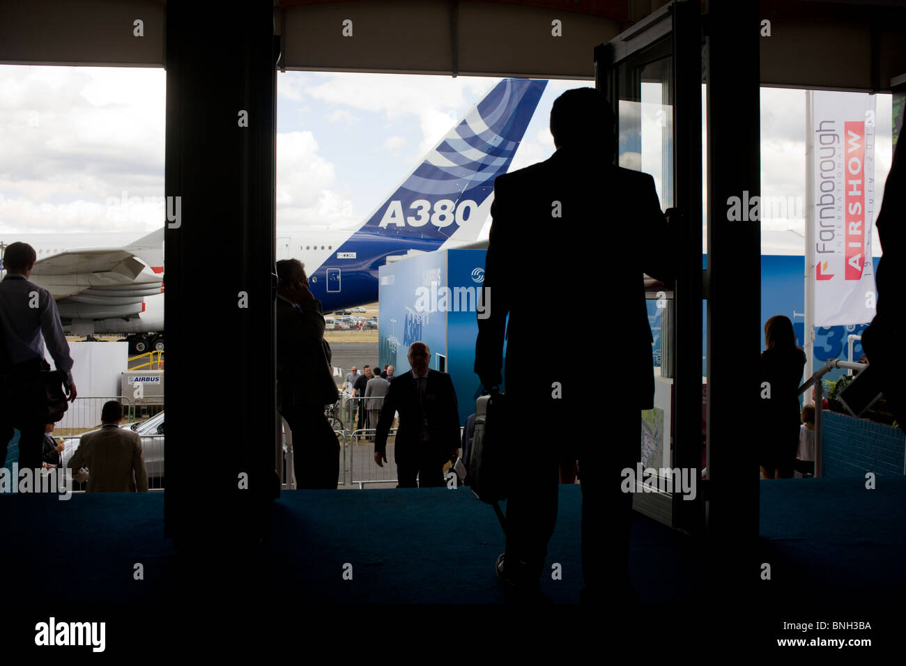 Busy visitors and delegates exit and enter the Farnborough Airshow with the massive Airbus A380 tail in the background. Stock Photo