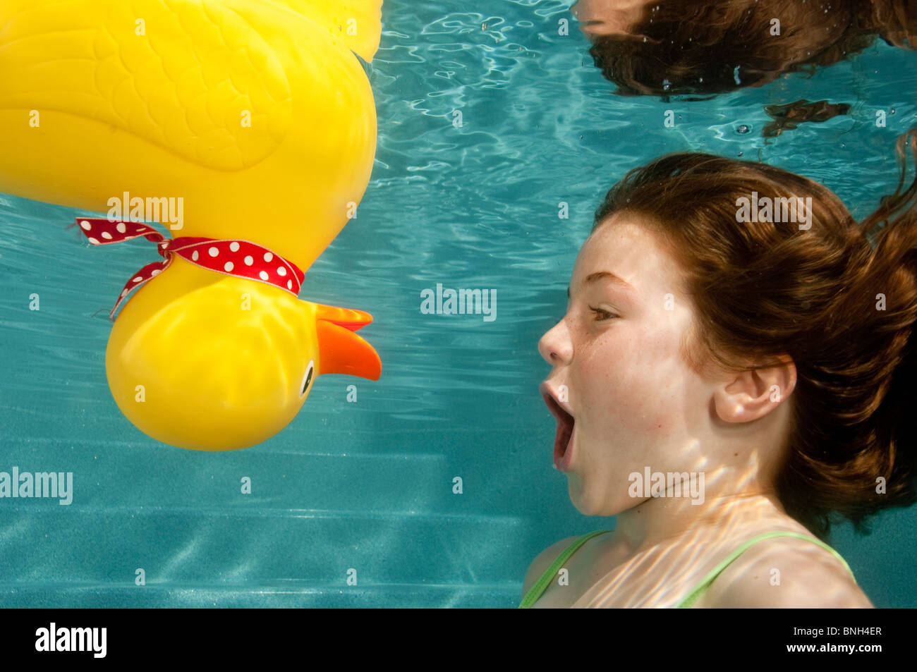 litle girl playing underwater with large yello rubber duck Stock Photo