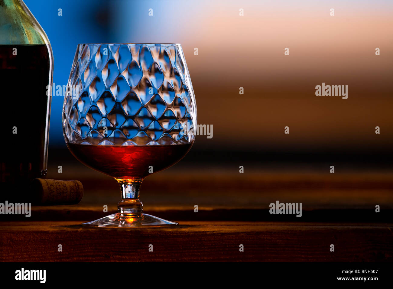 brandy snifter with bottle and cork on rough wood with soft focus background Stock Photo