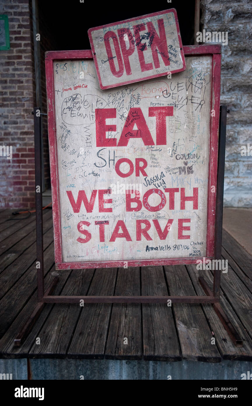 A funny sign stating 'Eat or We Both Starve' outside of Taylor Grocery Catfish Restaurant in Taylor, Mississippi. Stock Photo