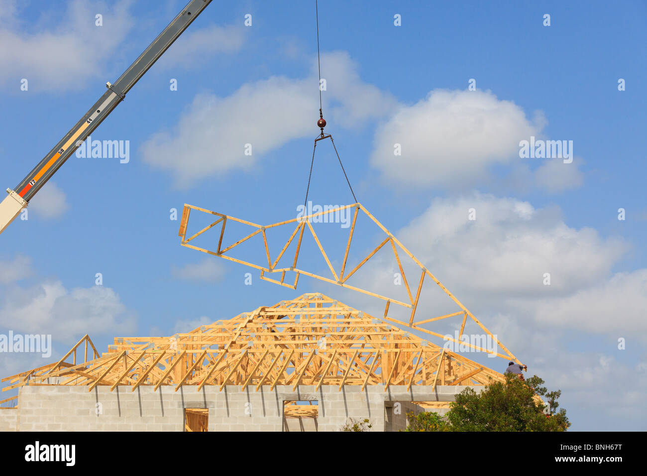 Roof Truss hanging from a crane being installed onto a new roof. Blue sky with clouds in background. Stock Photo