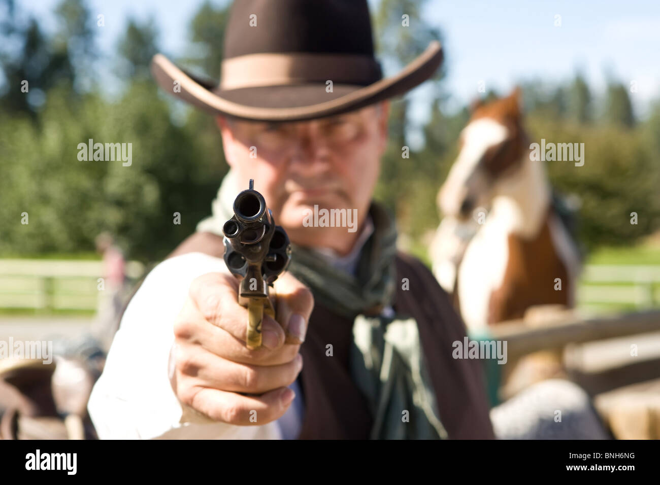 Cowboy aiming gun, focus only on gunpoint, horse in background Stock Photo