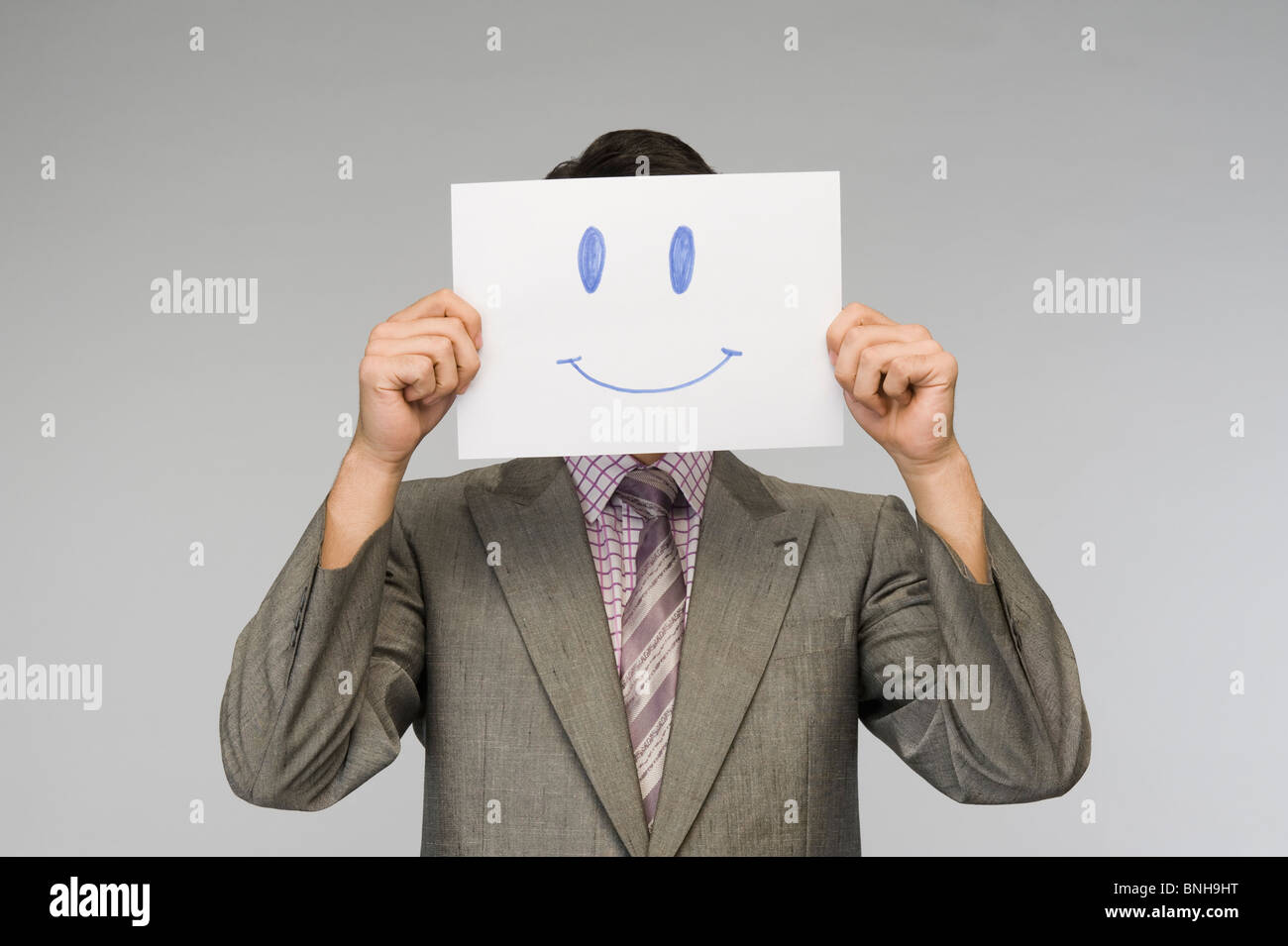 Businessman holding a smiley face paper in front of his face Stock Photo
