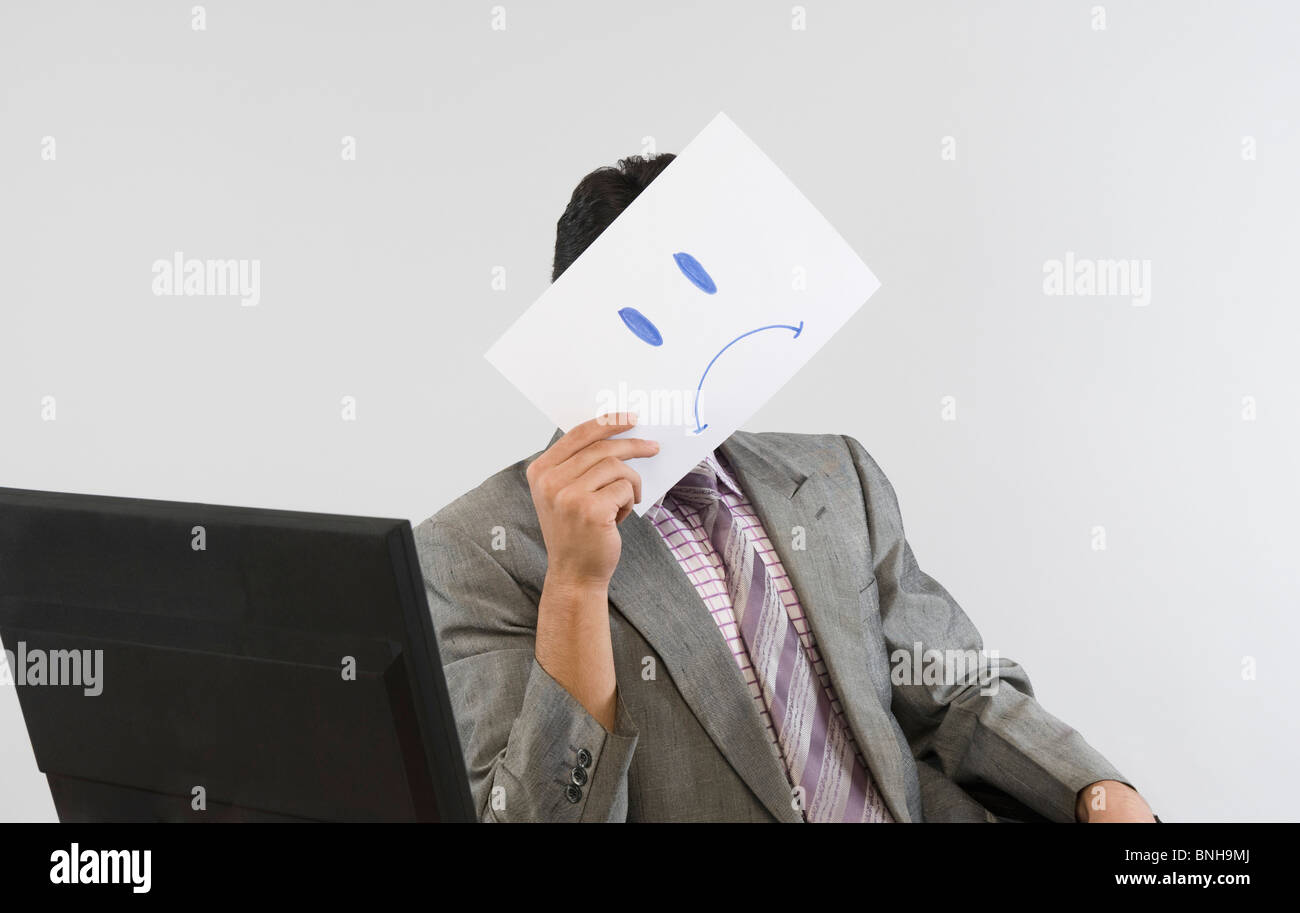 Businessman holding a smiley face paper in front of his face Stock Photo