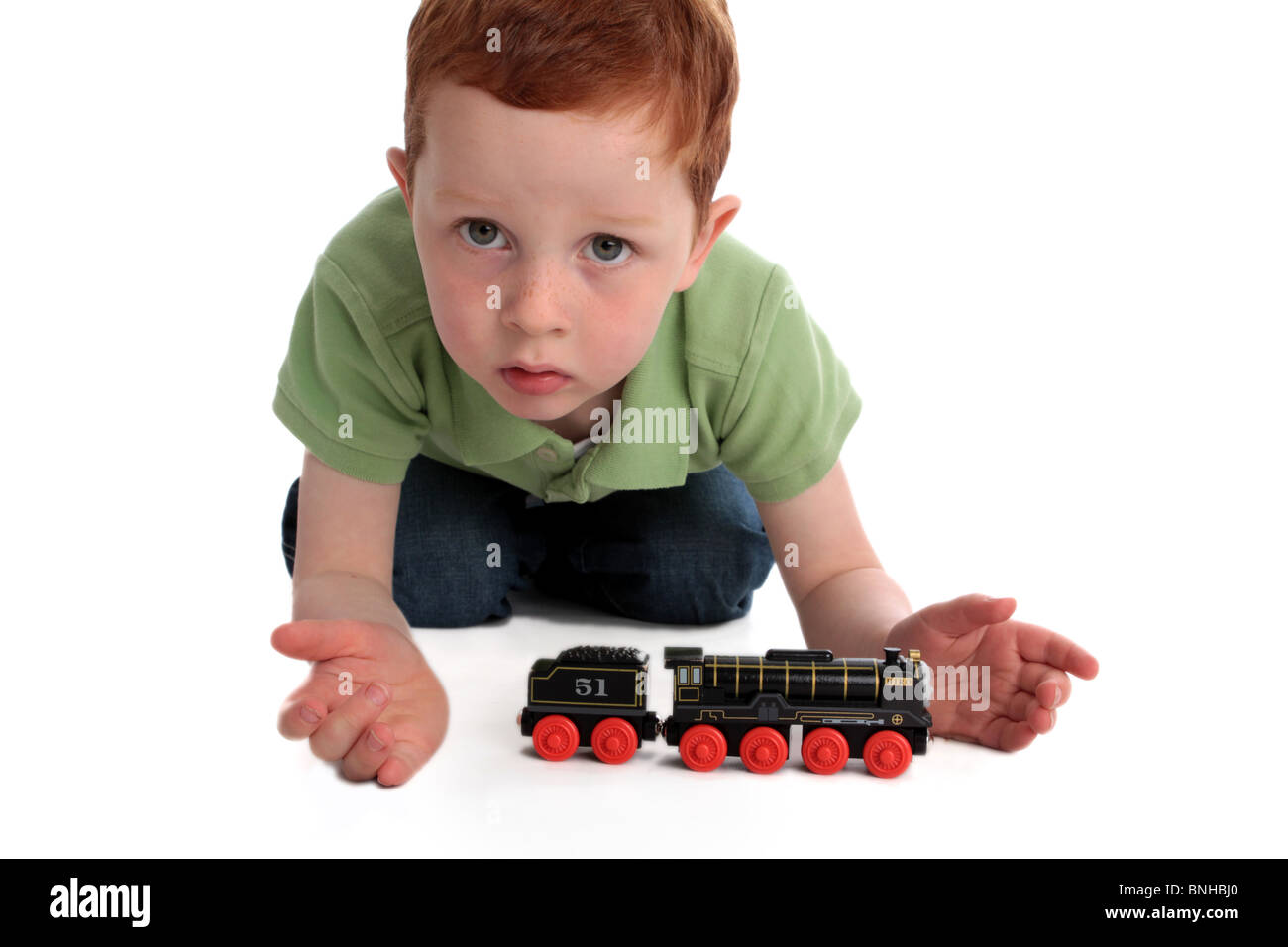 small red haired child playing with toy train on white background asking a question gesture Stock Photo