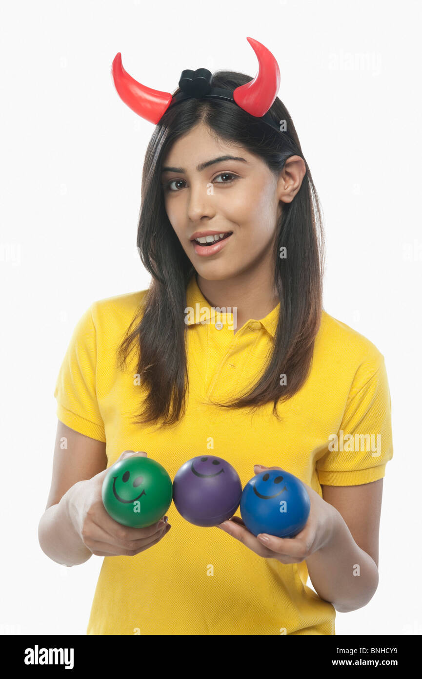 Portrait of a woman wearing devil's horns and holding smiley face balls Stock Photo