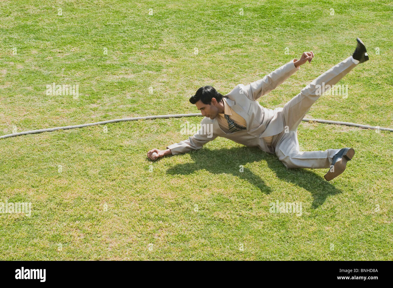 Businessman diving to stop a ball near boundary line in a cricket field