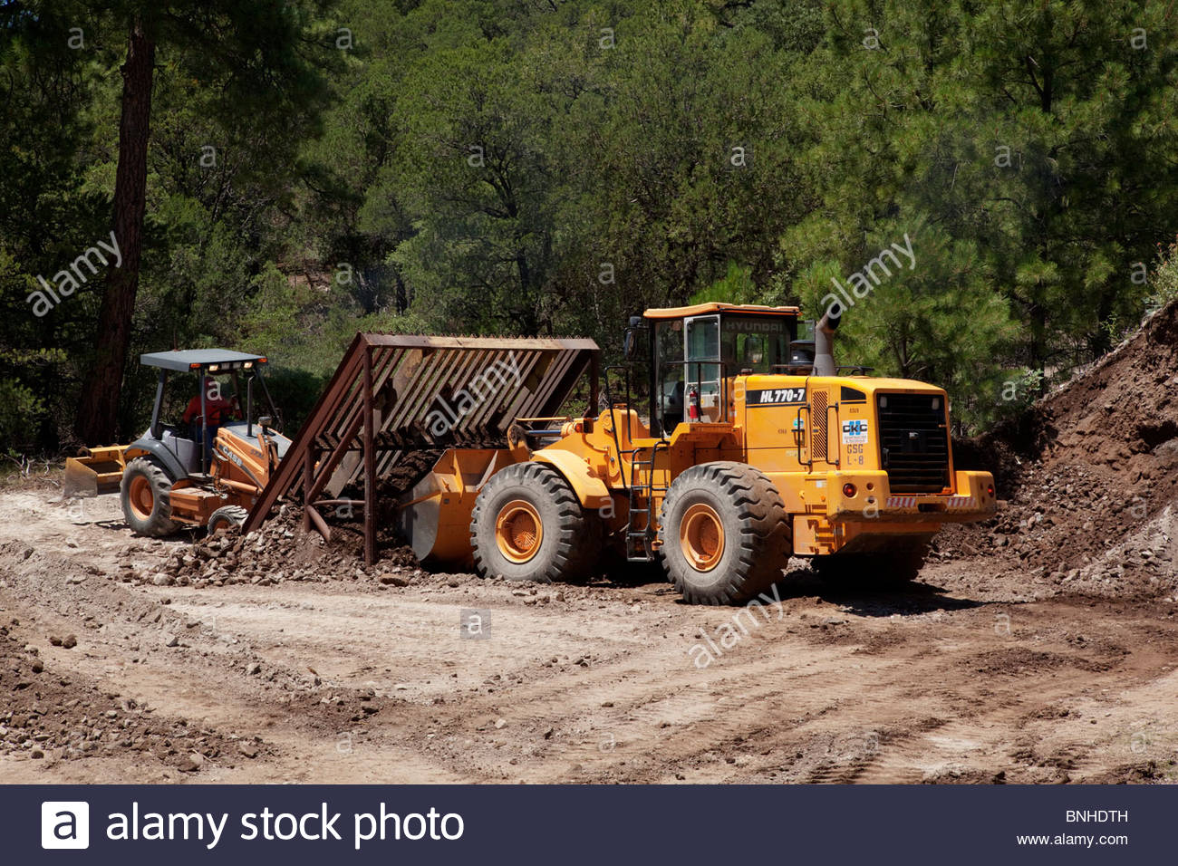 Hyundai hl770-7 wheel loader screening material on grizzly Case Backhoe  loader handling oversize 2 operators visible in cabs
