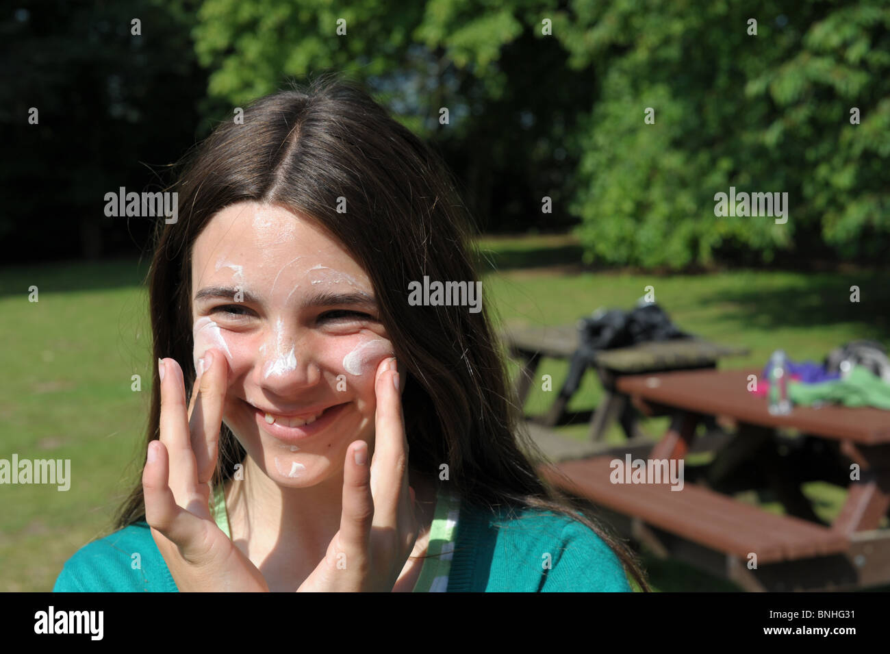 Girl happily applying suncream to protect her face from sunburn in a park on a hot sunny day Stock Photo