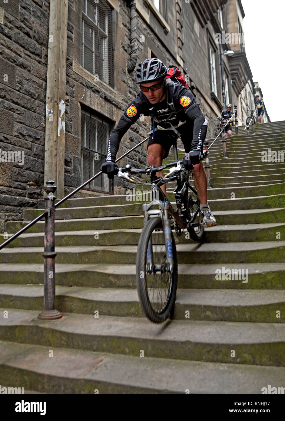 Male Competitor in Rat Race Edinburgh riding mountain bike down stairs steps in extreme adventure event Scotland UK Europe Stock Photo