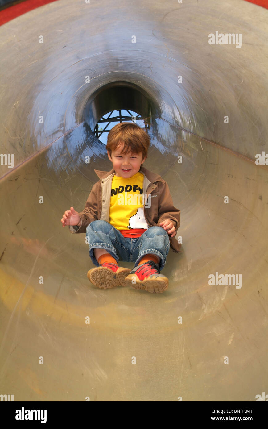 Child one boy sliding slide tunnel fun happy play playground playing children Stock Photo