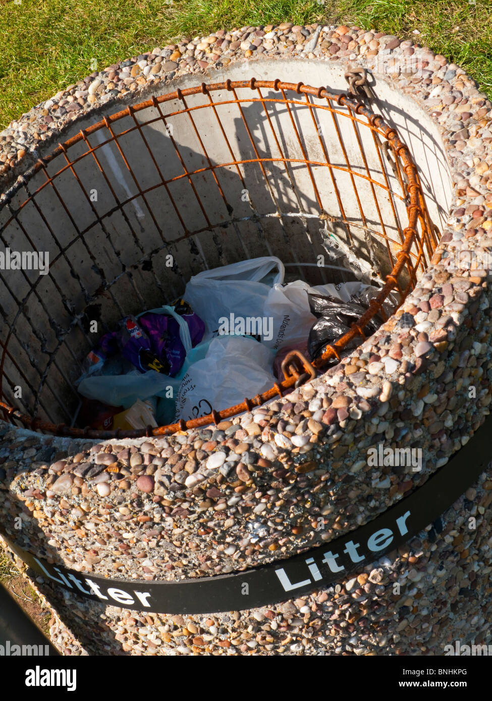 Close up view of concrete litter bin with rubbish placed in the internal wire basket Stock Photo
