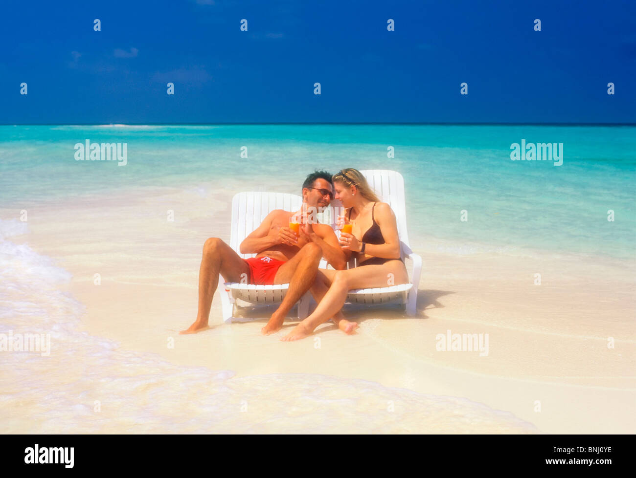 Pair Couple 20 30 vacation holidays travel Maldives beach seashore deck chair bikini drink sea water man husband woman waves Stock Photo