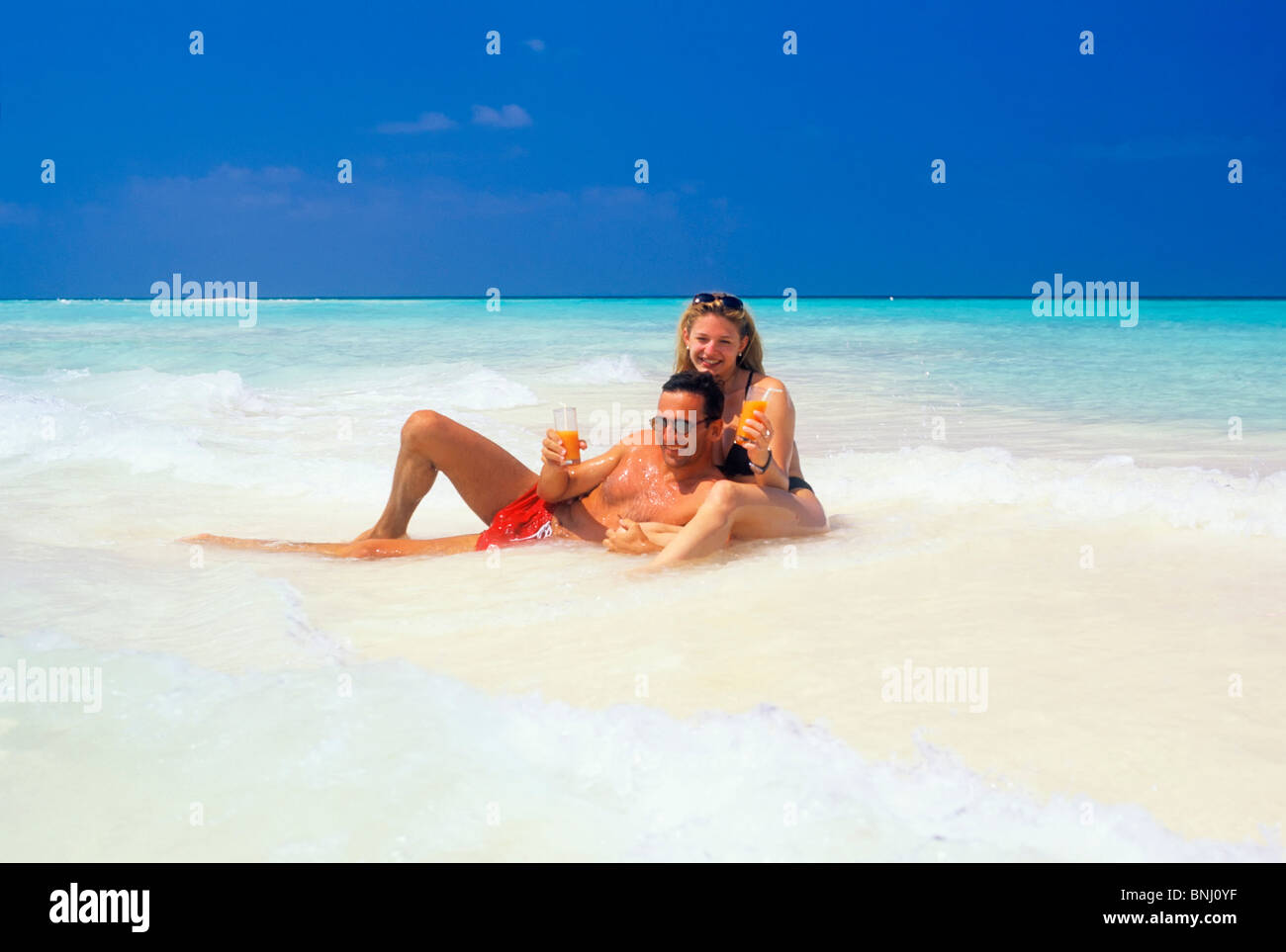 Pair Couple 20 30 vacation holidays travel Maldives beach seashore have a bath bikini drink sea water man husband woman waves Stock Photo