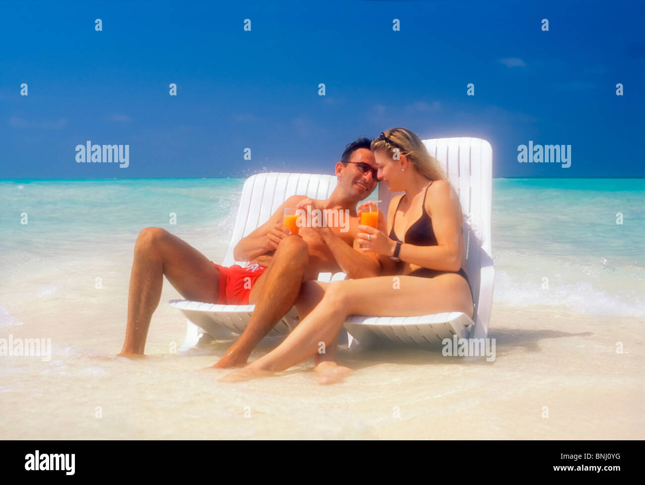 Pair Couple 20 30 vacation holidays travel Maldives beach seashore deck chair bikini drink sea water man husband woman waves Stock Photo