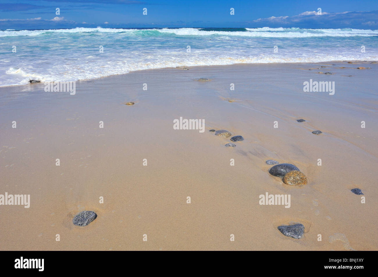 Romantic beach turquoise blue waves ebb flow on sandy shore with stones rocks horizon over water and reflections in sand Stock Photo