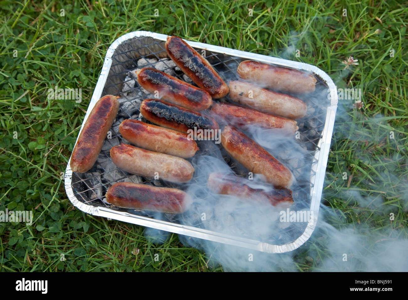 Sausages on disposable barbecue Stock Photo Alamy