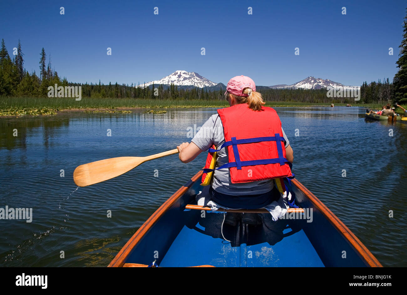 A woman in a life jacket paddles a canoe on Hosmer Lake along the Cascade Lakes Highway in the Oregon Cascades Stock Photo