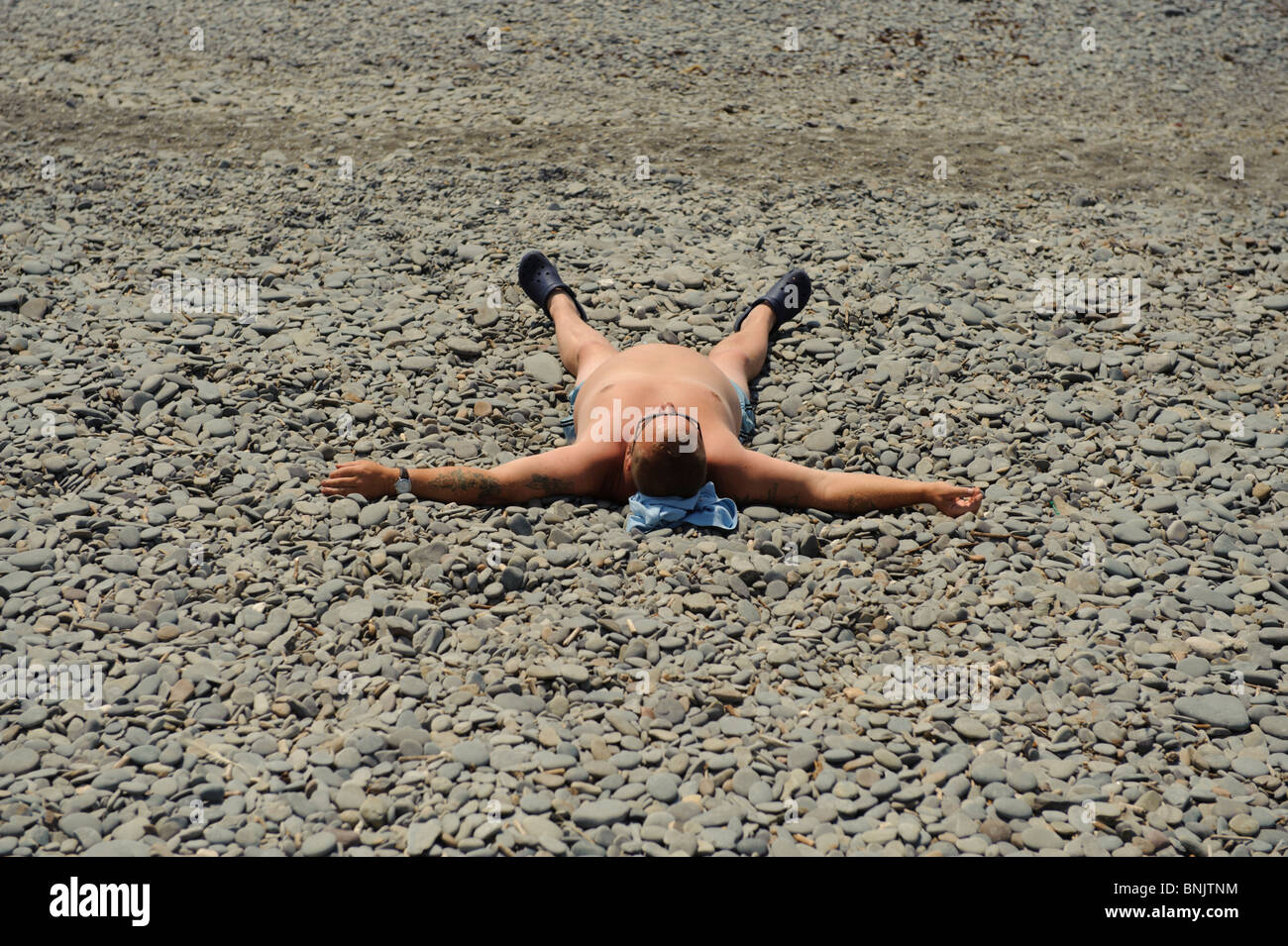 A man sunbathing alone lying spreadeagled  on the beach , Aberystwyth Wales UK Stock Photo