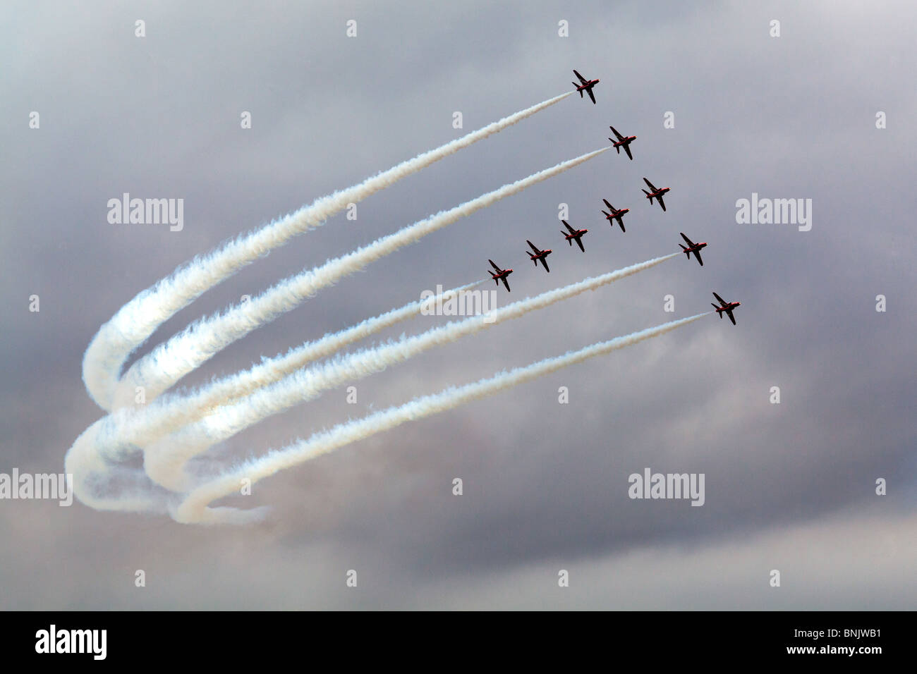 The Red Arrows in T Formation during an air display with white vapour trails showing up clearly against a grey sky at Fairford, Gloucestershire, UK Stock Photo