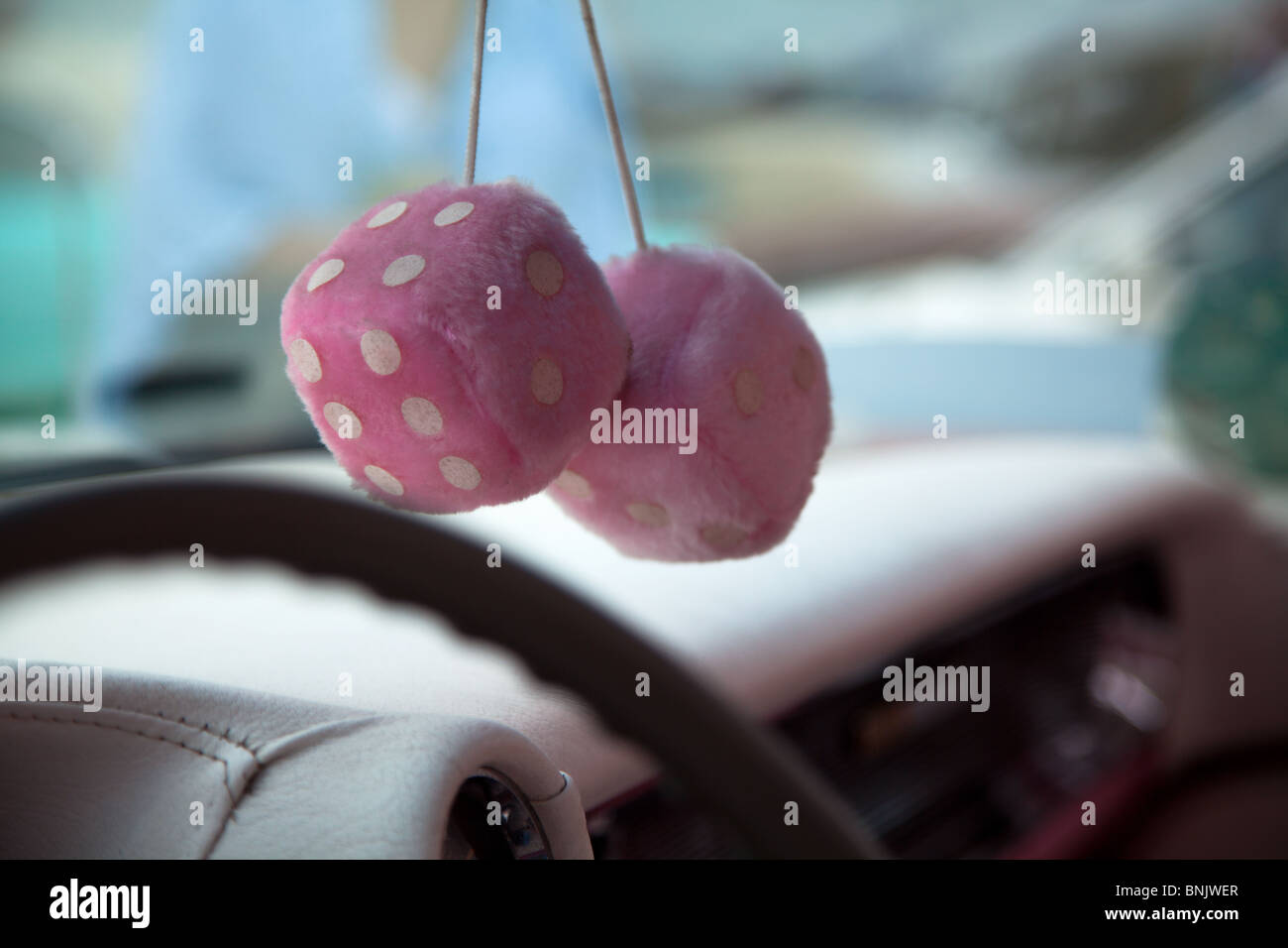 A close up shot of a pair of Pink fluffy furry dice hanging from the rear view mirror in an old car at Fairford, Gloucestershire, UK Stock Photo