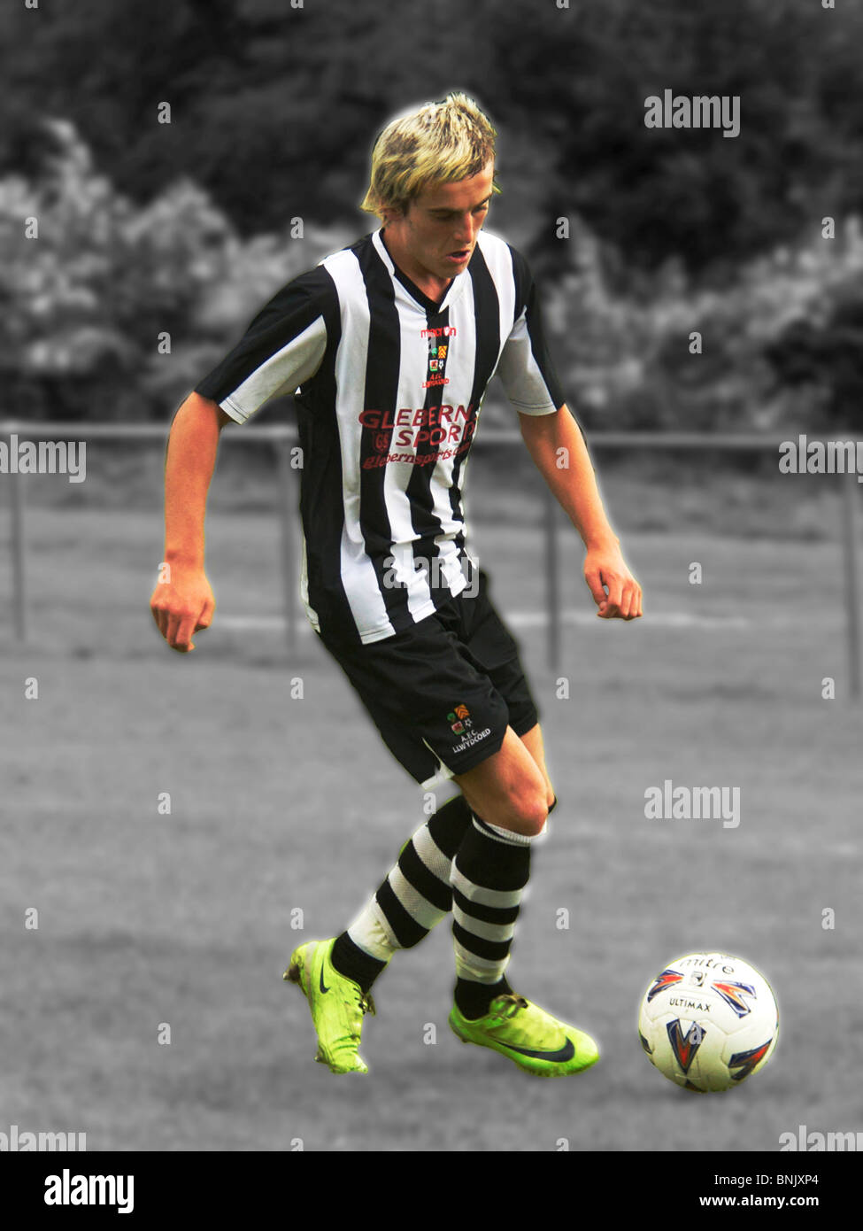 A footballer with yellow boots and a black & white background, the ball is at his feet, blond, stripped, hoops Stock Photo