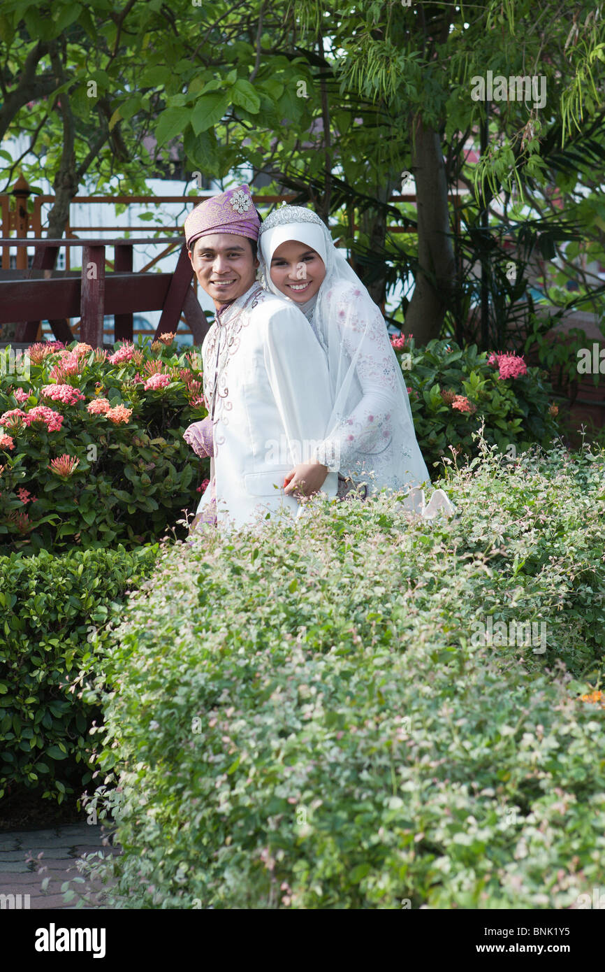 A malay bride and groom in traditional costume pose amongst the flowers in Malacca Malaysia Stock Photo