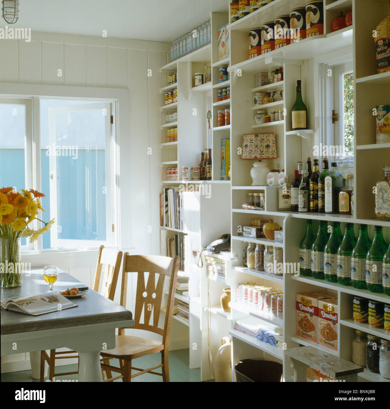 Wall of white shelves with bottles and cans in small white dining area of traditional kitchen Stock Photo